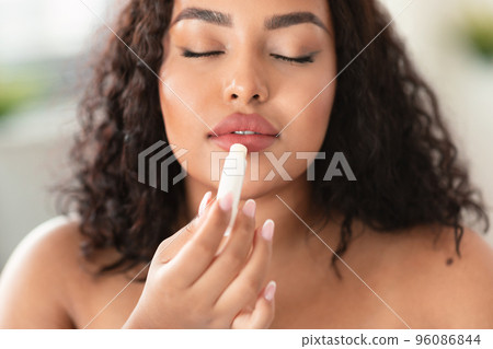 Young african american chubby lady applying lip balm, moisturizing and caring for skin, closeup shot 96086844