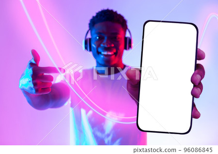 Positive black guy pointing at cell phone, using wireless headphones Positive black guy pointing at cell phone, using wireless headphones 96086845