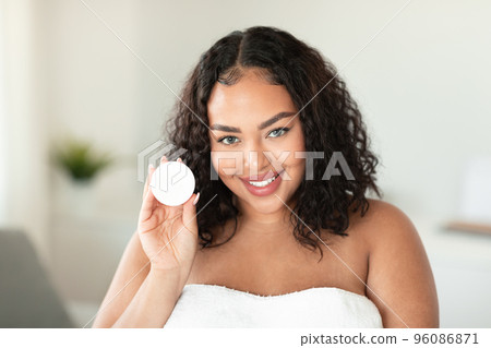 Skin treatments. Happy african american chubby woman holding open jar with cream and smiling at camera 96086871