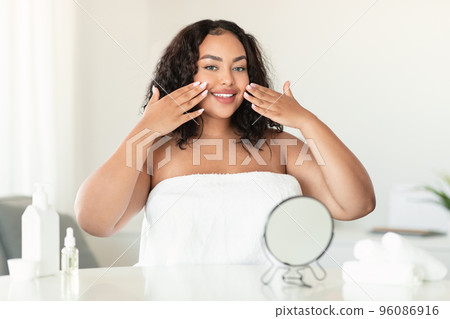Young african american plus size lady touching her face while making facial treatments in bedroom, copy space Young african american plus size lady touching her face while making facial treatments in bedroom, copy space 96086916