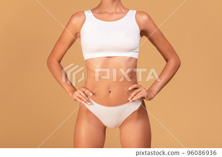 Unrecognizable well-fit caucasian woman in white underwear demonstrating her perfect body, posing over beige background 96086936