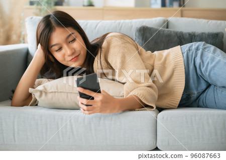 Happy young asian woman relax on comfortable couch at home texting messaging on smartphone 96087663
