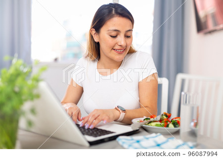 Woman working on laptop before eating vegetable salad Woman working on laptop before eating vegetable salad 96087994