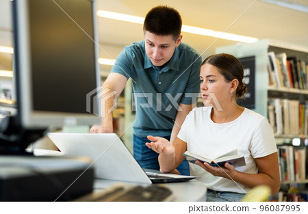 Man in casual clothes asking young lady to be more quiet while she is reading books in the library Man in casual clothes asking young lady to be more quiet while she is reading books in the library 96087995