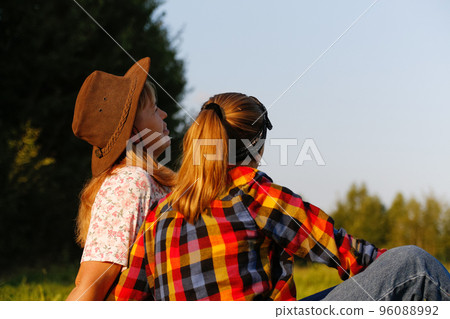 Defocus back view of mother and daughter sitting on meadow and looking at green field. Friendship love concept. Woman and girl summer background. Out of focus Defocus back view of mother and daughter sitting on meadow and looking at green field. Friendship love concept. Woman and girl summer background. Out of focus 96088992