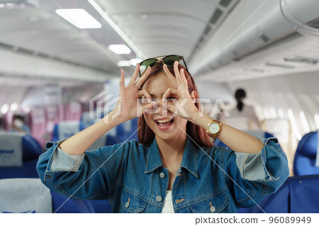 Portrait of an Asian woman taking a selfie or capturing memories while waiting for an economy class flight. Travel concept, vacations, tourism. 96089949