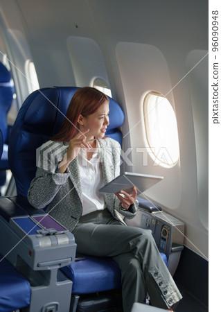 portrait of A successful asian businesswoman or female entrepreneur in formal suit in a plane sits in a business class's seat and uses a tablet computer during flight. 96090948