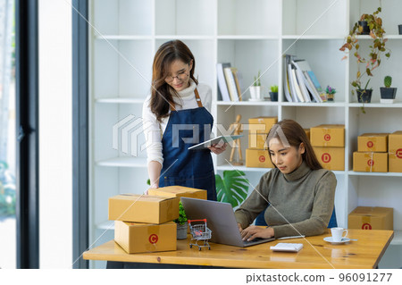 two happy women selling products online Start a small business owner using a laptop computer and tablet to calculate prices and prepare for postage 96091277