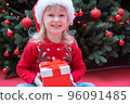 Happy little child kid girl in Santa red hat holding Christmas gift in hand. 96091485