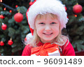 Happy little child kid girl in Santa red hat holding Christmas gift in hand. 96091489