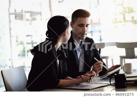 At the consultation, a male adviser uses a pen to point at a tablet to explain the profit restructuring to female business owners 96091873