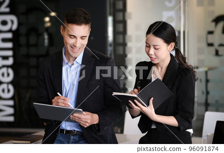 At the consultation, a male adviser uses a pen to point at a tablet to explain the profit restructuring to female business owners 96091874