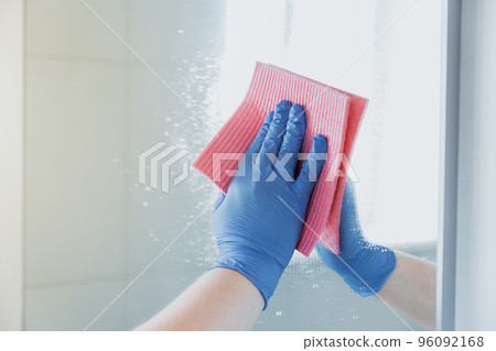 Cropped view of housekeeper woman hand in blue rubber glove polishing, cleaning, swiping mirror with cloth rag, spraying cleaner liquid while cleaning bathroom at home. Housekeeping, cleaning service 96092168