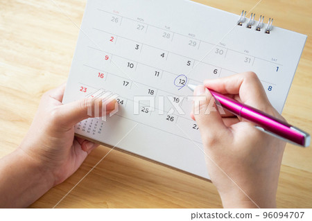 calendar page with female hand holding pen on desk table calendar page with female hand holding pen on desk table 96094707
