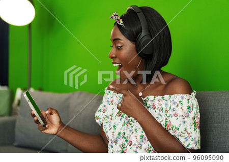 African woman listening to music with headphones while sitting on couch at home African woman listening to music with headphones while sitting on couch at home 96095090