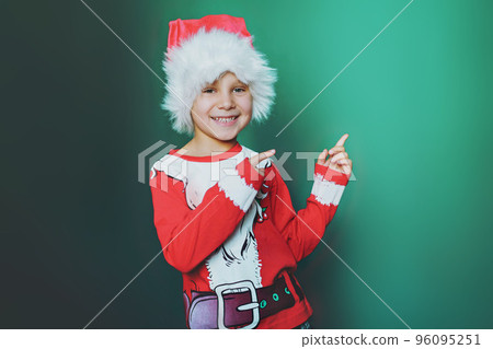 happy smiling caucasian boy in santa tee shirt and hat pointing to blank space on whitebackground happy smiling caucasian boy in santa tee shirt and hat pointing to blank space on whitebackground 96095251