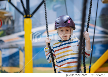 caucasian boy climbing in adventure park passing obstacle course. high rope park indoors 96095253