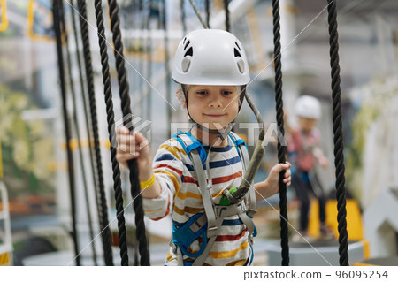 caucasian boy climbing in adventure park passing obstacle course. high rope park indoors caucasian boy climbing in adventure park passing obstacle course. high rope park indoors 96095254