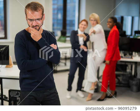 A middle-aged man is upset because of the ridicule of his female colleagues. Discrimination against men in the office. A middle-aged man is upset because of the ridicule of his female colleagues. Discrimination against men in the office. 96095279