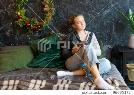 Thoughtful caucasian girl enjoying christmas eve at home using smart phone 96095372