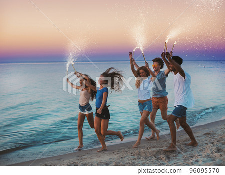 Happy smiling friends running at the beach with sparkling candles Happy smiling friends running at the beach with sparkling candles 96095570