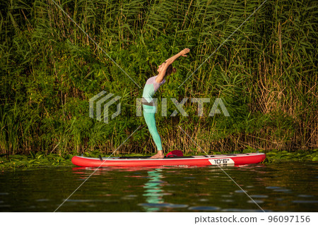 Young woman are doing yoga on a stand up paddle board SUP on a beautiful lake or river Young woman are doing yoga on a stand up paddle board SUP on a beautiful lake or river 96097156