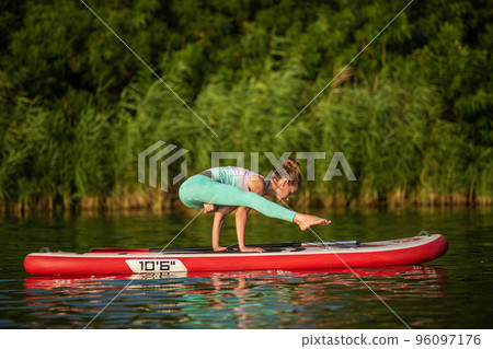 Young woman are doing yoga on a stand up paddle board SUP on a beautiful lake or river 96097176