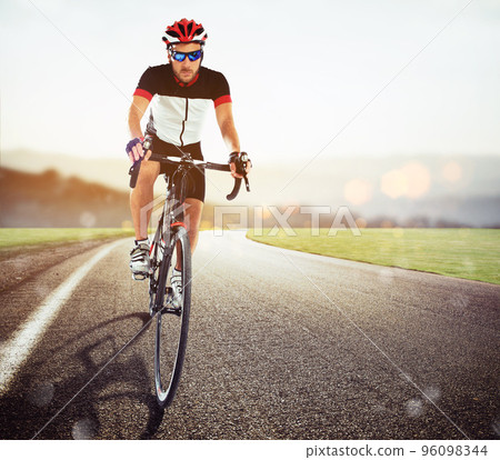 Cyclist racing on the road at sunset 96098344