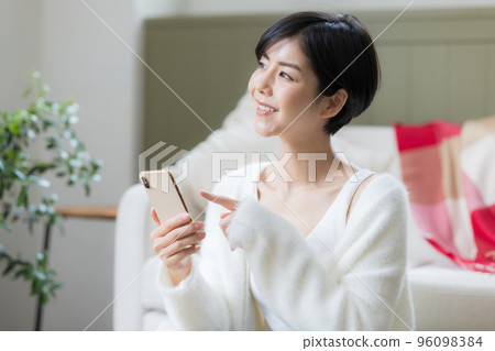 A woman sitting on the floor in the living room looking at her smartphone A woman sitting on the floor in the living room looking at her smartphone 96098384