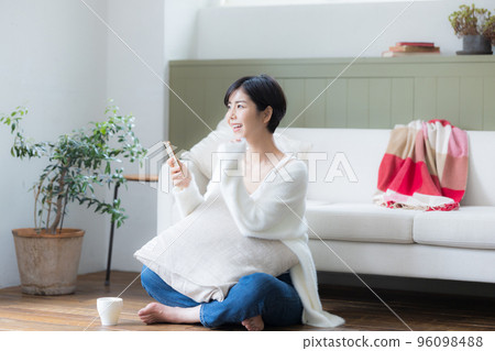 一個女人坐在客廳的地板上,看著她的智能手機 一個女人坐在客廳的地板上,看著她的智能手機 96098488