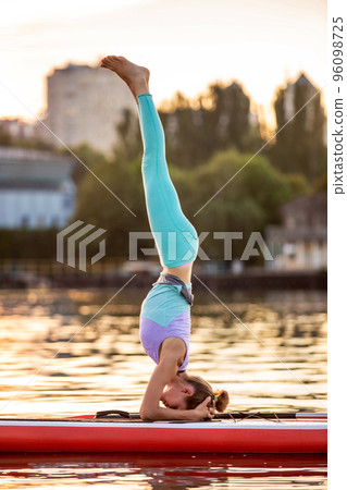 Sporty woman in yoga position on paddleboard, doing yoga on sup board, exercise for flexibility and stretching of muscles 96098725