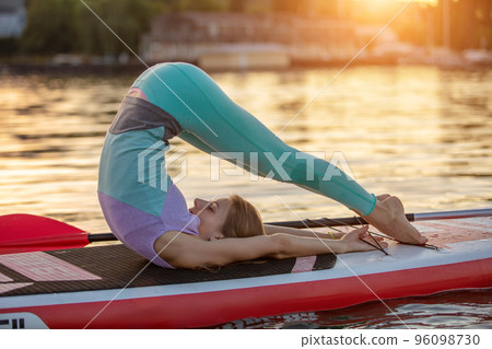 Sporty woman in yoga position on paddleboard, doing yoga on sup board, exercise for flexibility and stretching of muscles Sporty woman in yoga position on paddleboard, doing yoga on sup board, exercise for flexibility and stretching of muscles 96098730