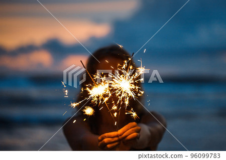 Woman with sparklers on the beach at sunset Woman with sparklers on the beach at sunset 96099783