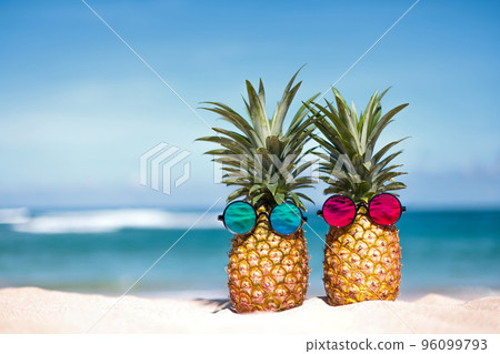Creative tropical pineapple pair in sunglasses on sandy beach Creative tropical pineapple pair in sunglasses on sandy beach 96099793