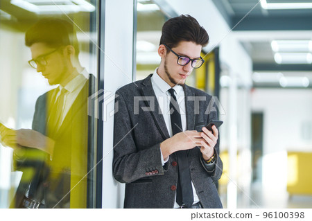 Young office worker in glasses using mobile smart phone. Businessman holds telephone in hand. 96100398