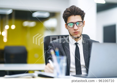 Young office manager working with papers and computer working at office. Man in a suit working. Young office manager working with papers and computer working at office. Man in a suit working. 96100710