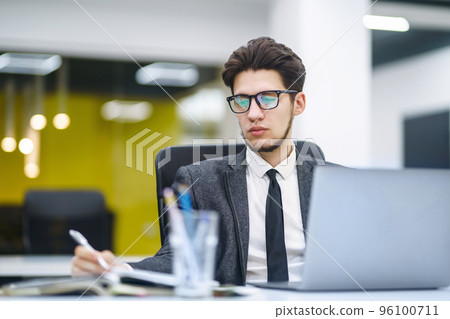 Young office manager working with papers and computer working at office. Man in a suit working. Young office manager working with papers and computer working at office. Man in a suit working. 96100711