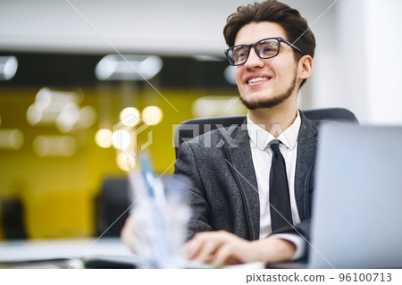 Young office manager working with papers and computer working at office. Man in a suit working. Young office manager working with papers and computer working at office. Man in a suit working. 96100713