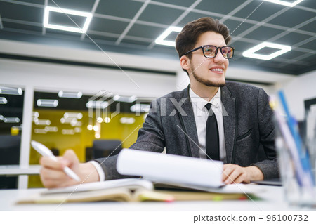 Young office manager working with papers and computer working at office. Man in a suit working. 96100732