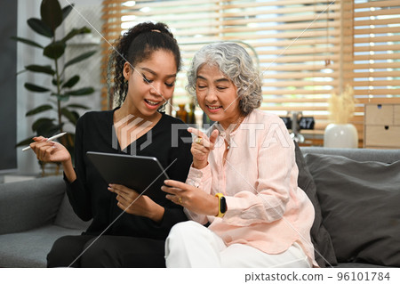 Smiling young woman teaching interested elderly mother how to use a tablet or shows some application. Elderly, technology concept Smiling young woman teaching interested elderly mother how to use a tablet or shows some application. Elderly, technology concept 96101784