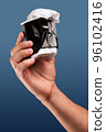 Male hand holds, raised black crumpled paper cup of tea or coffee. 96102416