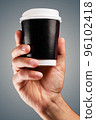 Male hand holds, raised black paper cup of tea or coffee. 96102418