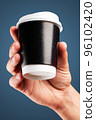 Male hand holds, raised black paper cup of tea or coffee. 96102420