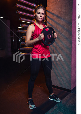 Girl athlete keeps the disc from the bar weighting agent for doing crossfit and fitness. Girl athlete keeps the disc from the bar weighting agent for doing crossfit and fitness. 96102426