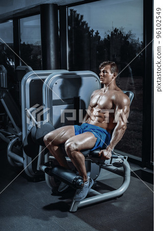Good looking man doing leg extensions on a machine at the gym 96102549
