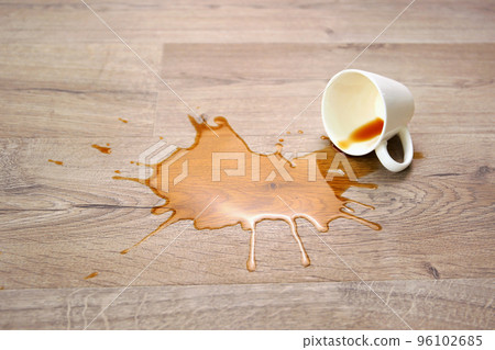 A cup of coffee fell on laminate, coffee spilled on floor. Focus on the puddle. 96102685