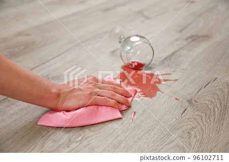 Glass of red wine fell on laminate, wine spilled on floor. A woman wipes the laminate from moisture. Glass of red wine fell on laminate, wine spilled on floor. A woman wipes the laminate from moisture. 96102711