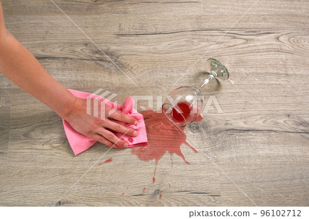 Glass of red wine fell on laminate, wine spilled on floor. A woman wipes the laminate from moisture. Glass of red wine fell on laminate, wine spilled on floor. A woman wipes the laminate from moisture. 96102712