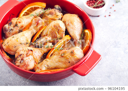 Chicken drumsticks with oranges and thyme baked in red round baking dish Chicken drumsticks with oranges and thyme baked in red round baking dish 96104195