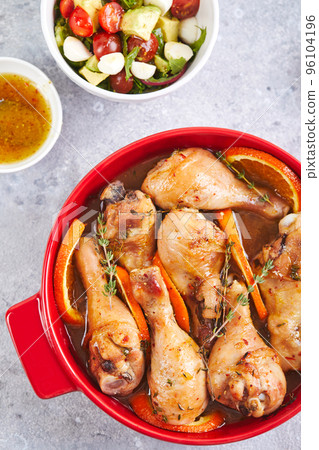 Chicken drumsticks with oranges and thyme baked in red round baking dish 96104196
